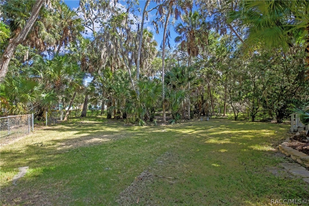 4737 S Sawmill Way, Homosassa, FL 34448 Wide grassy lot: oaks with Spanish moss, a white vinyl fence at the right, a house at the far right, plants at the left, and dappled shade across the grass.