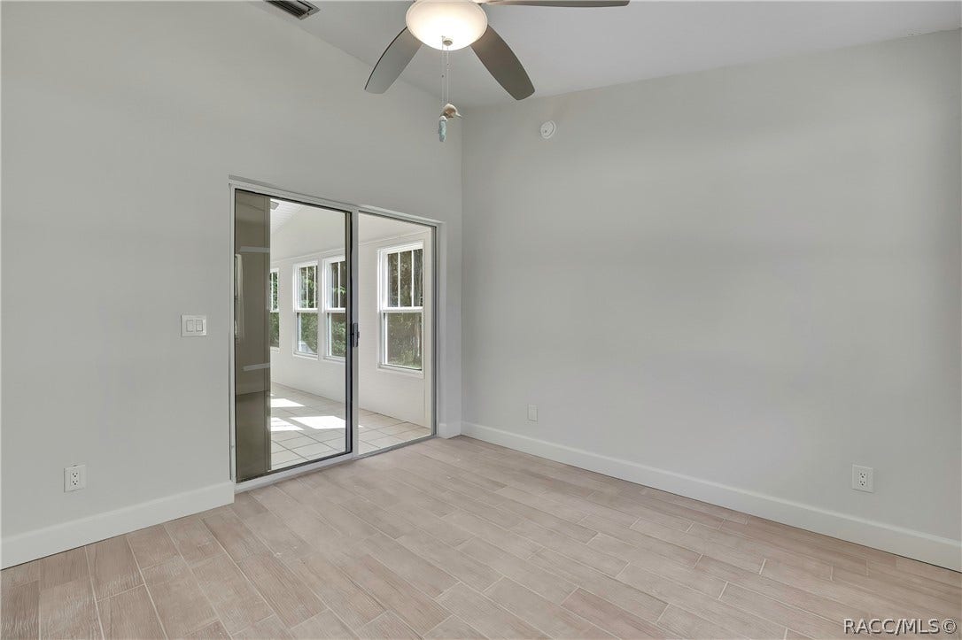 4737 S Sawmill Way, Homosassa, FL 34448 Empty bedroom: light plank tile floor, a sliding glass door at the left to the screened porch with a tiled porch floor and windows visible through it, a ceiling fan with a dome light at the top of the frame, white walls and wall outlets. No furniture.