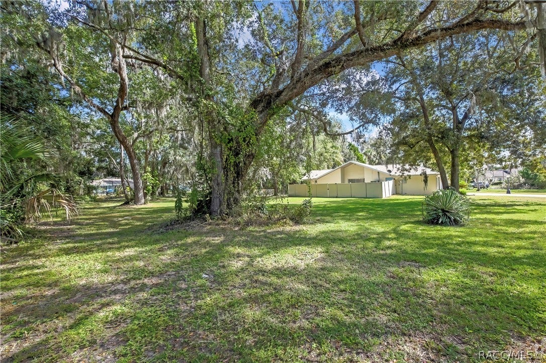 4737 S Sawmill Way, Homosassa, FL 34448 Wide grassy lot: oaks with Spanish moss, a white vinyl fence at the right, a house at the far right, plants at the left, and dappled shade across the grass.