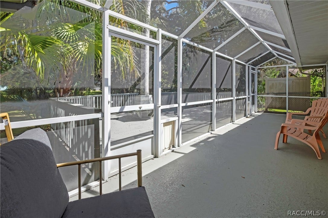 4737 S Sawmill Way, Homosassa, FL 34448 Wood deck: grey wood deck planks, railing, a built-in bench around a palm tree trunk, steps down to a fenced lawn, palm trees, oaks with Spanish moss, and a chain-link fence in the background.