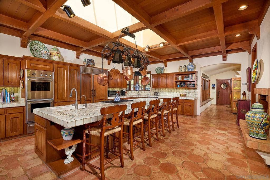The family style kitchen features custom wood cabinetry, a fireplace and an expansive Mexican tile island with built in gas range and sink.