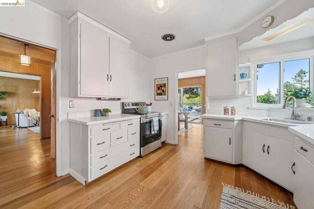 White cabinetry with dark hardware, stainless steel range, light-toned wood-finish flooring, and white countertops