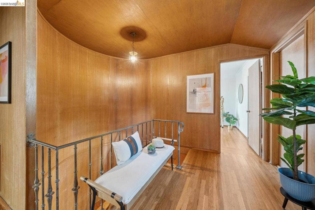 Wood-finish wall paneling, curved architectural details, wood flooring, wrought iron railing, and a ceiling-mounted light fixture