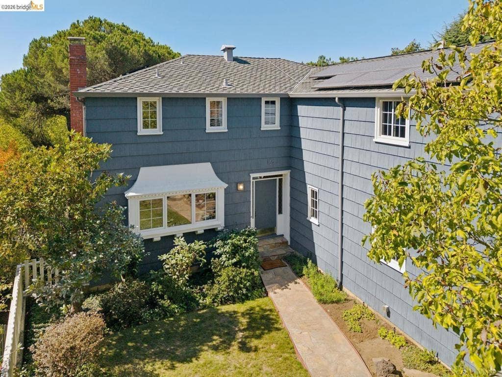 Shingle-sided exterior with a white-trimmed bay window and a stone pathway