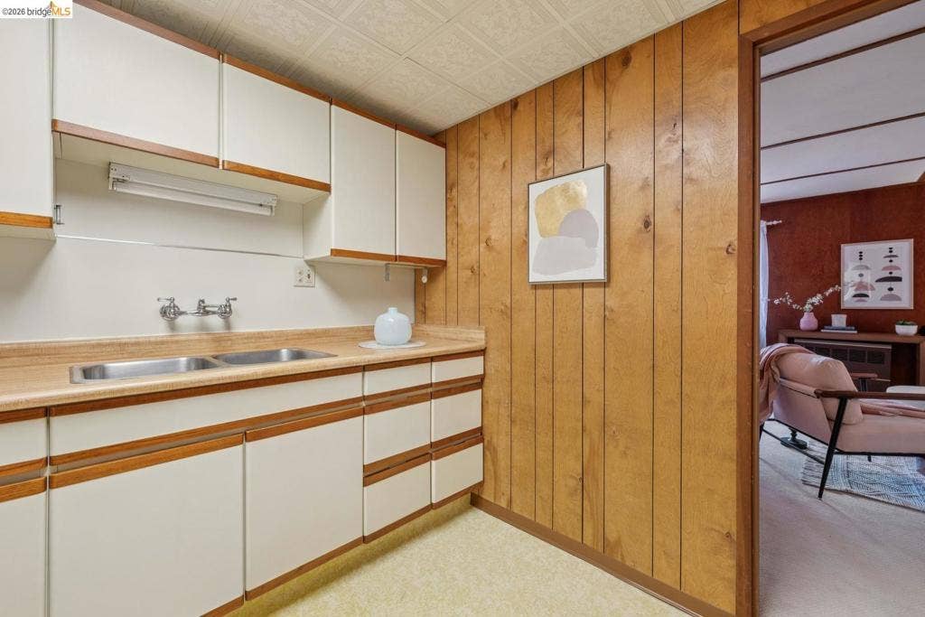 White upper and lower cabinetry with wood-finish trim, stainless steel double-basin sink, and a light-toned countertop