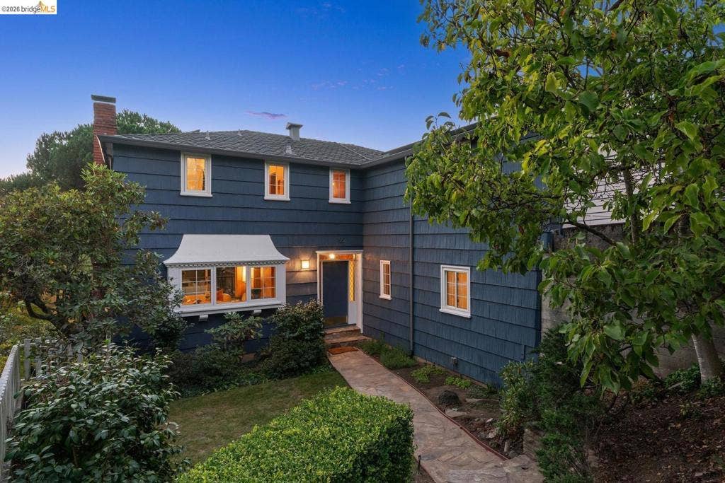 Two-story residence featuring blue siding, white trim windows, a prominent bay window, and a natural stone-paved walkway