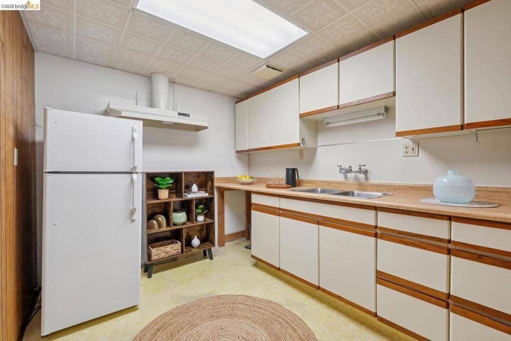 Cream-finished cabinetry with wood trim, a stainless steel double basin sink, and a white range hood