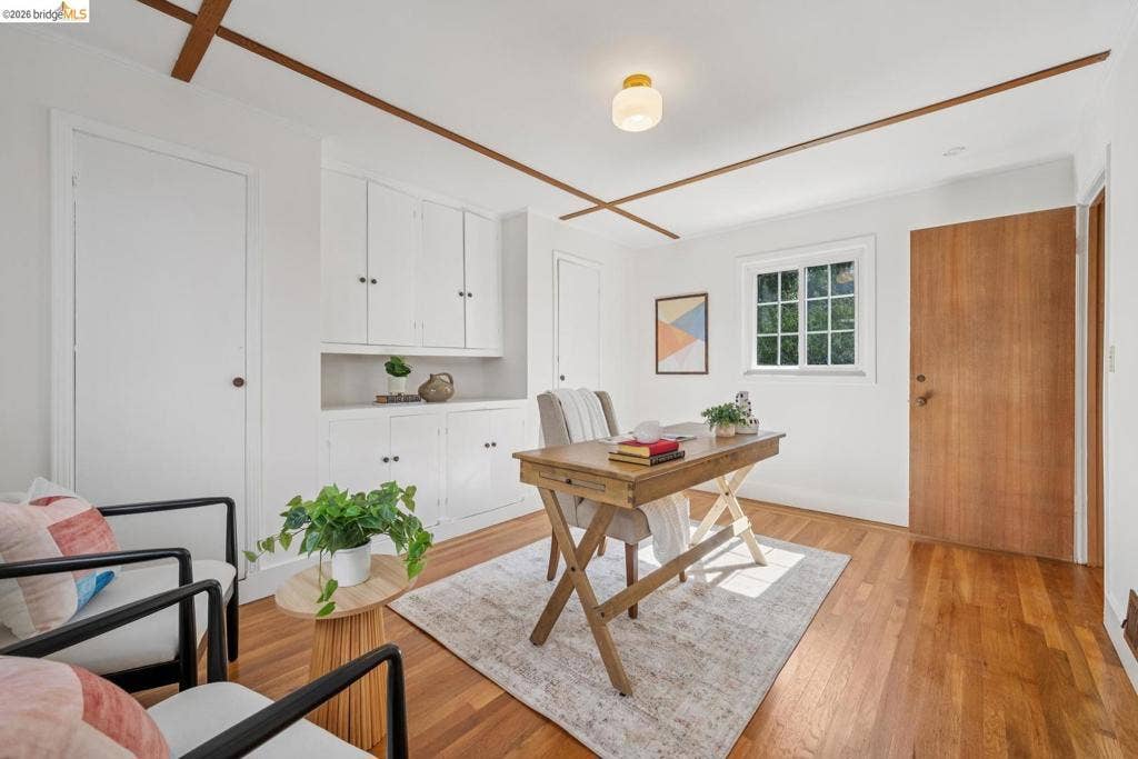 Hardwood flooring, white built-in cabinetry, window with multiple panes, wooden ceiling accents, and a flush-mount ceiling light