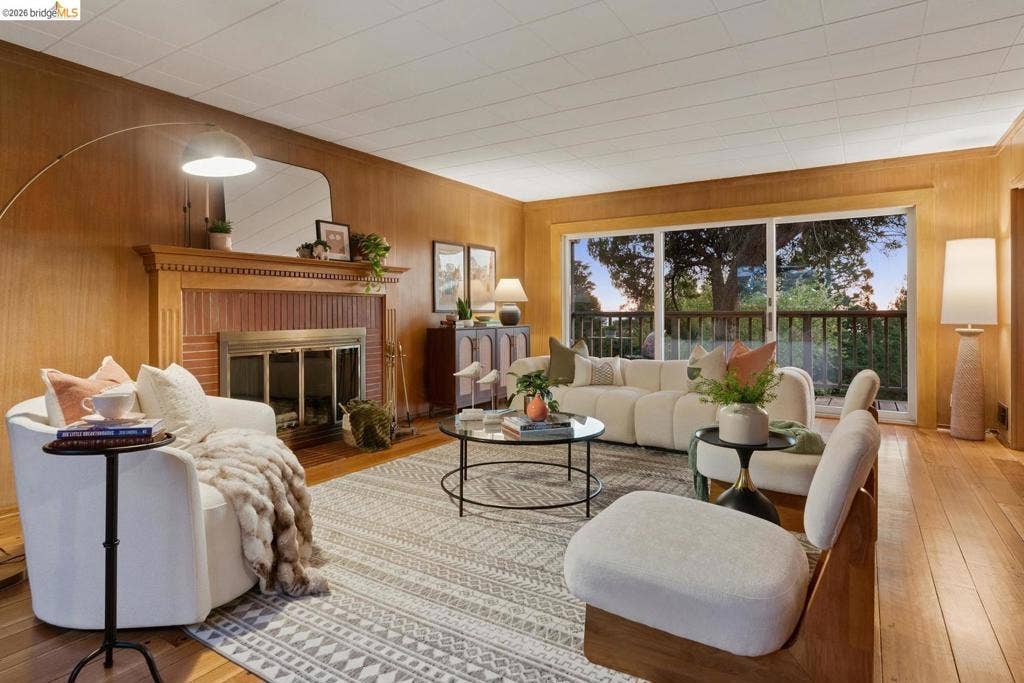 Warm wood paneling, brick fireplace with decorative mantel, wood-finish flooring, and expansive glass sliding doors
