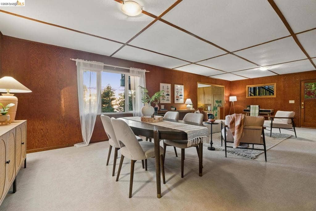 Textured wood paneling, grid-patterned ceiling, large window with outdoor scenery, recessed lighting, and carpeted flooring