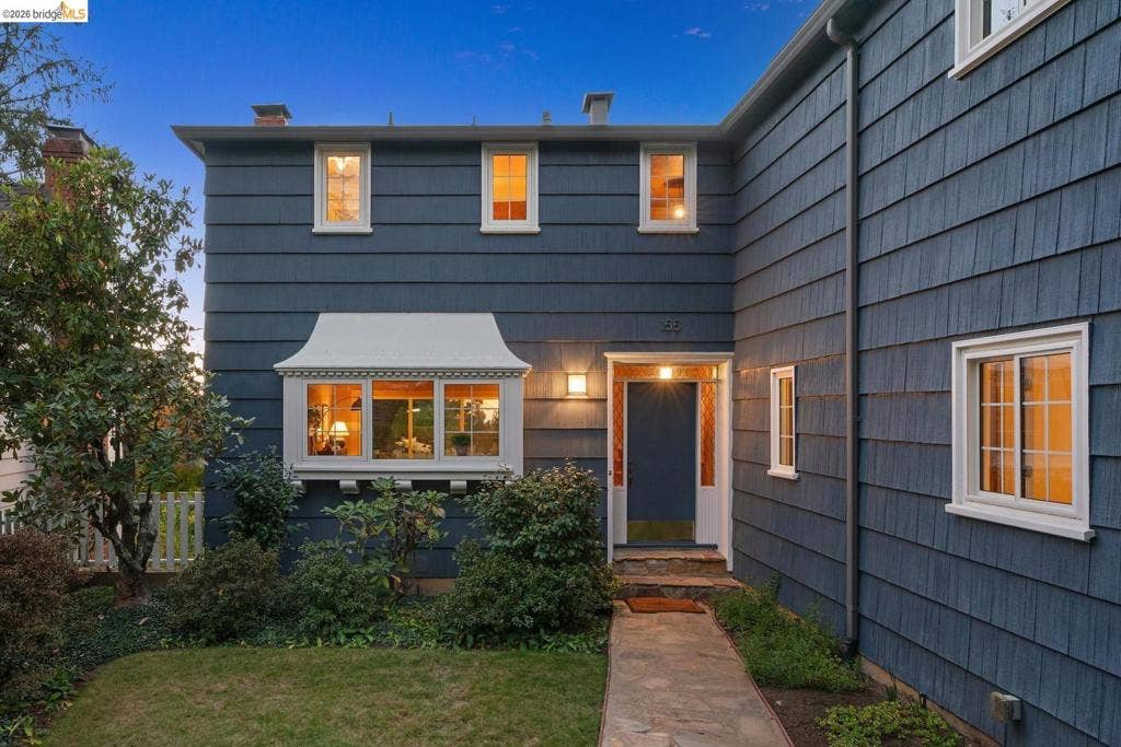 Shingle siding exterior with a prominent bay window featuring decorative trim, a walkway leading to a front entry, and multiple white-framed windows