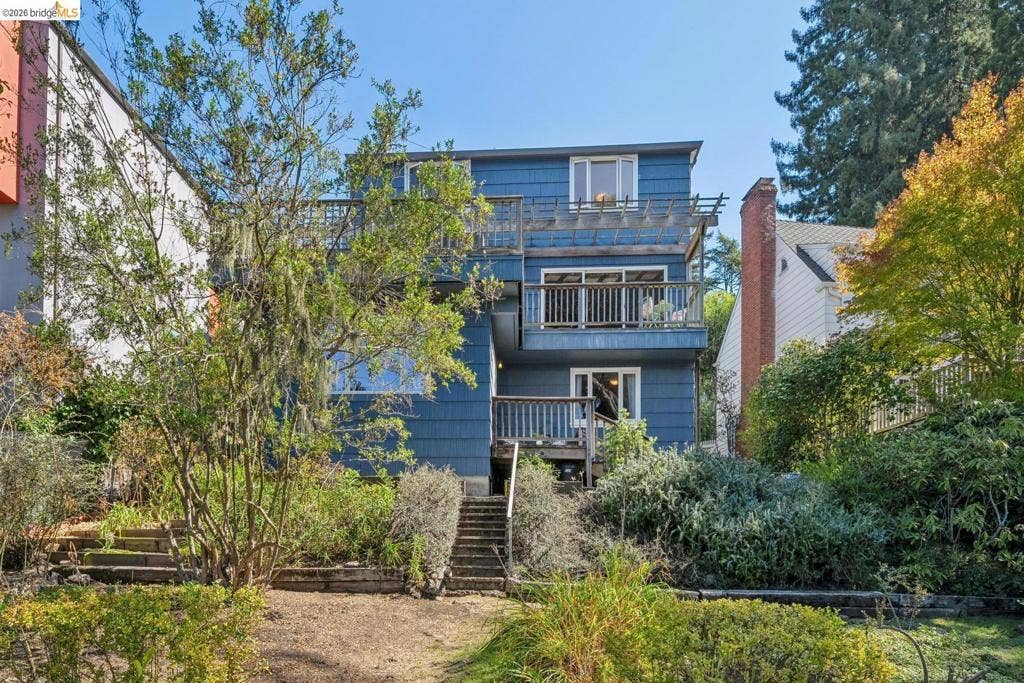 Multi-story residence featuring a blue exterior, multiple decks, and extensive landscaping