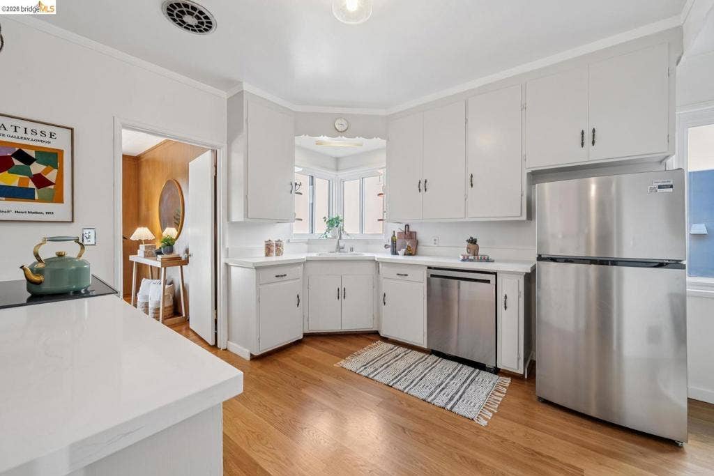 White cabinetry, stainless steel appliances, wood-finish flooring, white countertops, and a built-in corner sink