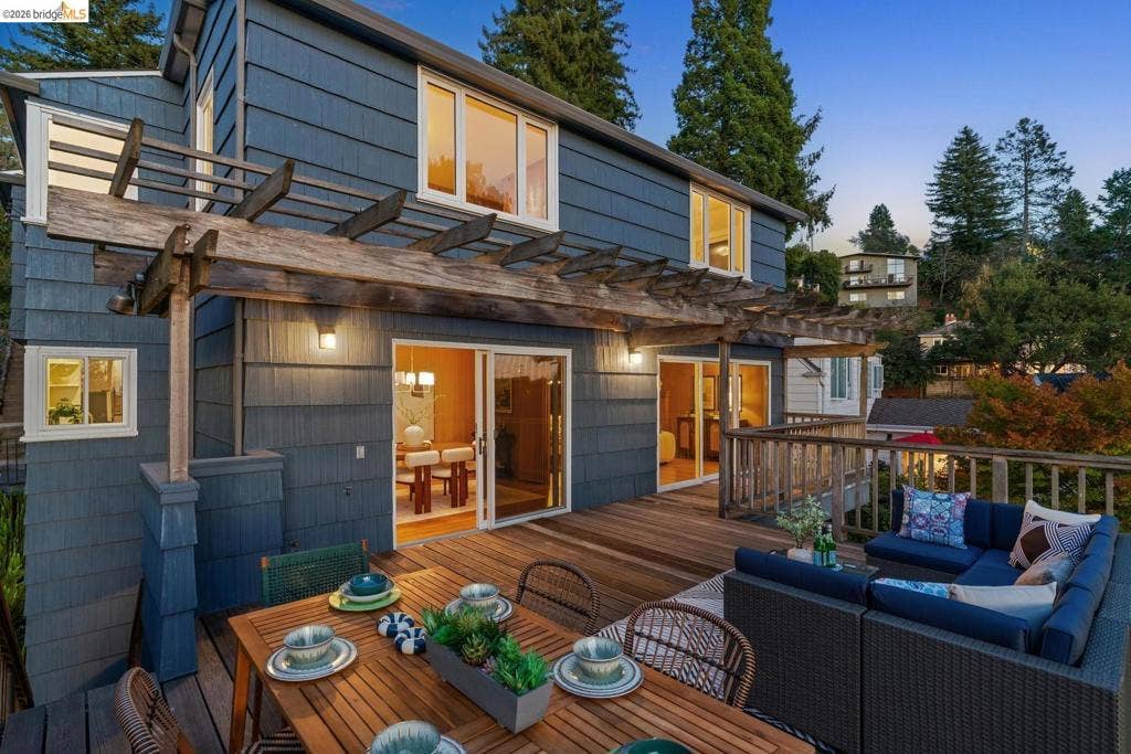 Spacious wood-finish deck with a pergola, featuring sliding glass doors, exterior lighting, and wood railing
