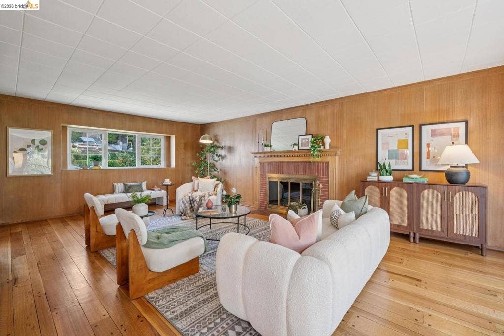 Wood-paneled walls, a brick-surround fireplace, light wood-finish flooring, and multi-pane windows