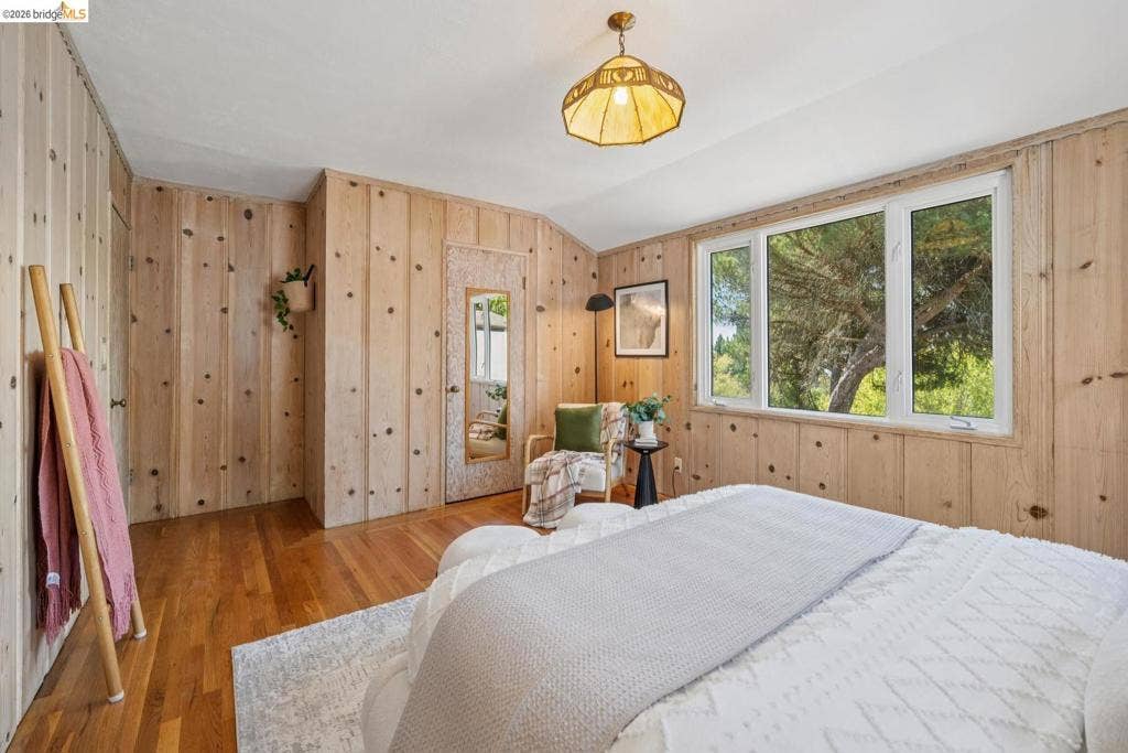 Wood-paneled walls, hardwood flooring, multiple windows, and a built-in recessed door with a mirror