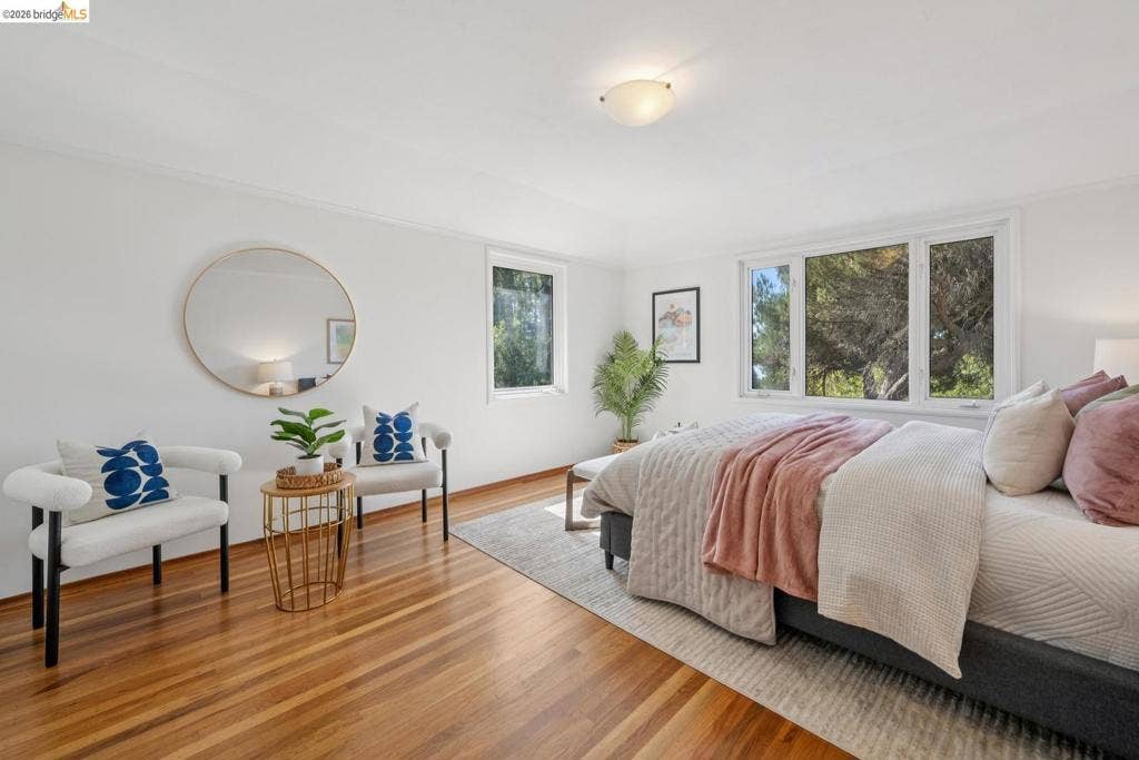 Warm wood-finish flooring, white walls, multiple windows, and a flush-mount ceiling light