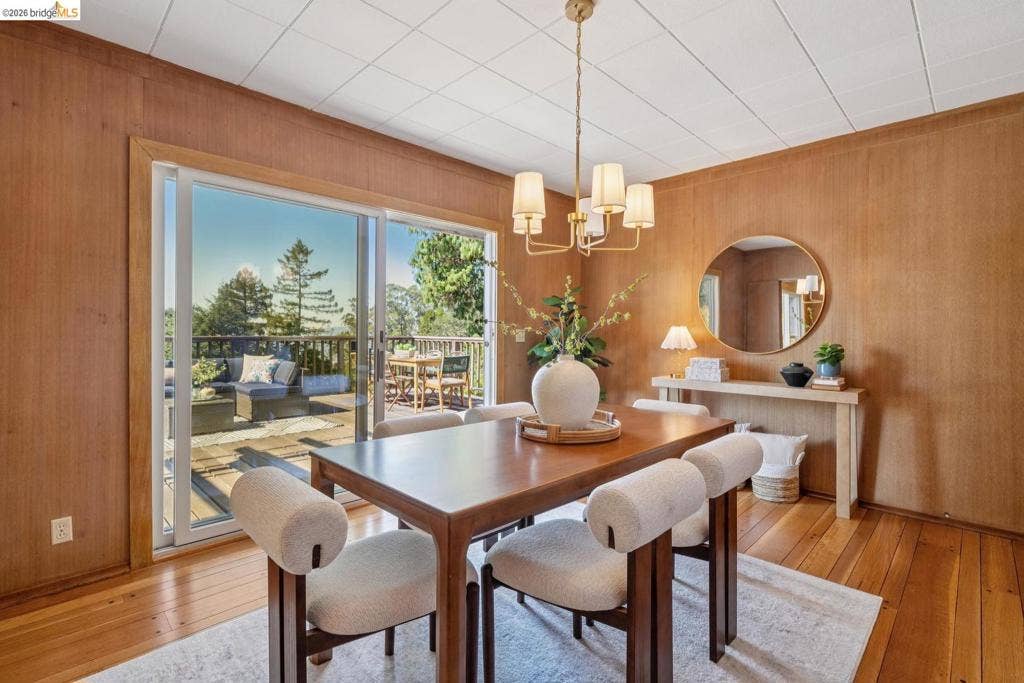 Hardwood flooring, wood-paneled walls, sliding glass door to exterior deck, and a brass-finish chandelier