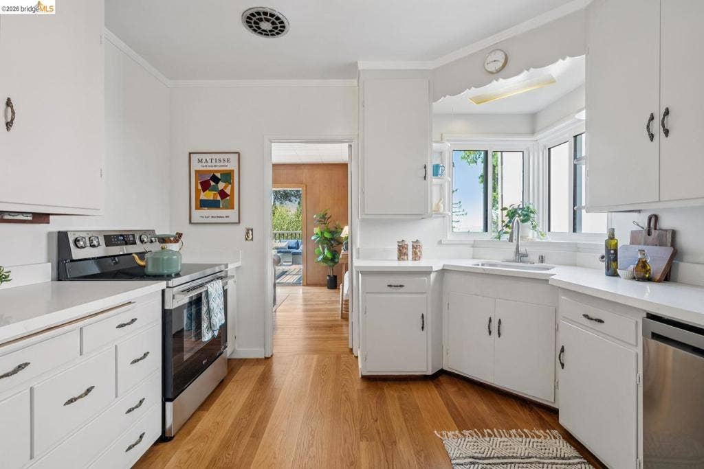 Kitchen featuring white cabinetry, light-toned countertops, wood-finish flooring, and a stainless steel oven