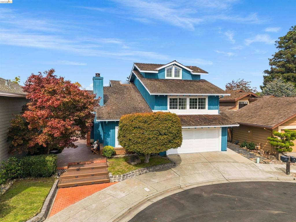 Multi-level residence featuring a two-car garage, brick paver walkway, and a prominent chimney
