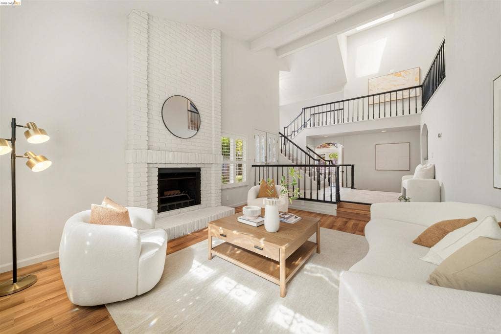 Two-story living area with hardwood flooring, a white brick fireplace, and a skylight