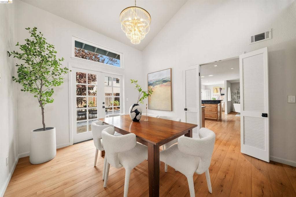 Vaulted ceiling with an ornate chandelier, French doors with transom window, wood-finish flooring, and louvered double doors