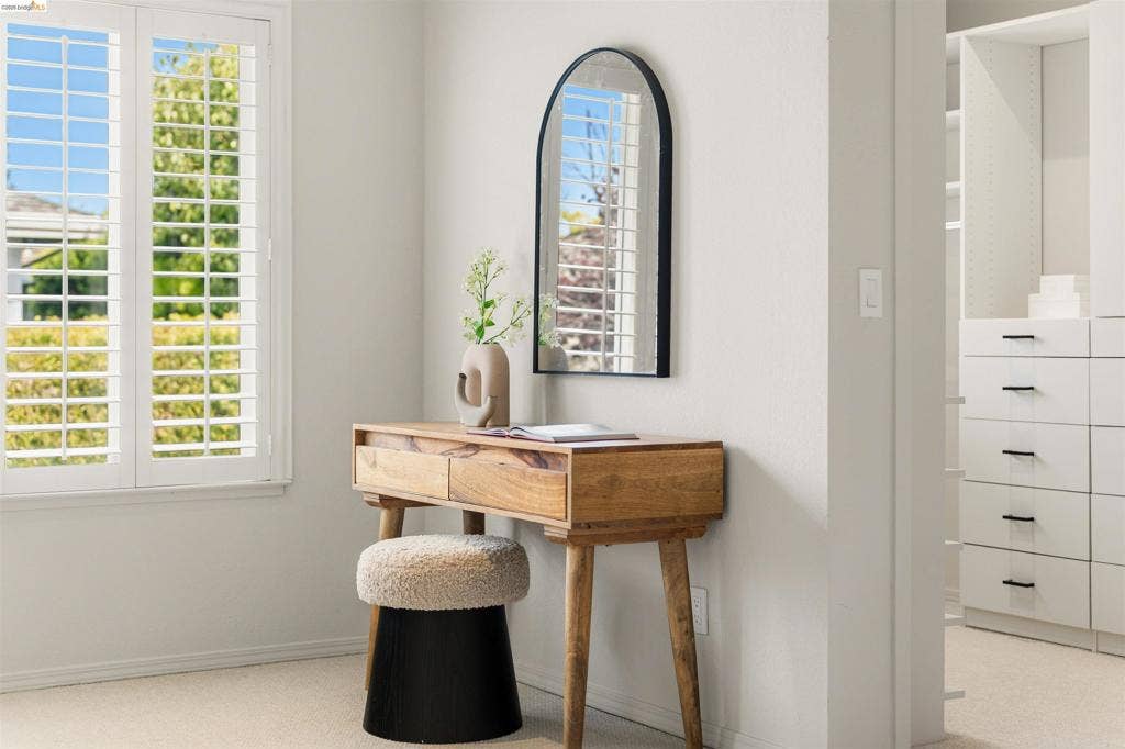 Window with white plantation shutters, light neutral wall paint, and built-in closet cabinetry with dark hardware