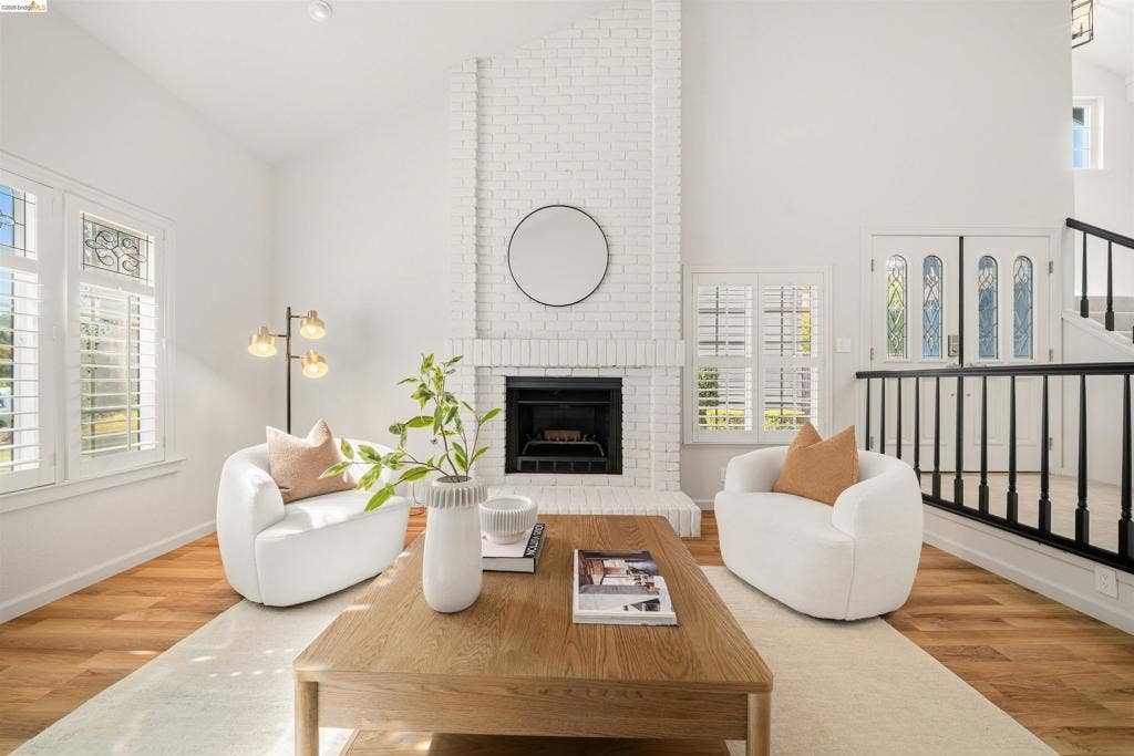 Vaulted ceiling with a white brick fireplace, wood-finish flooring, and white plantation shutters