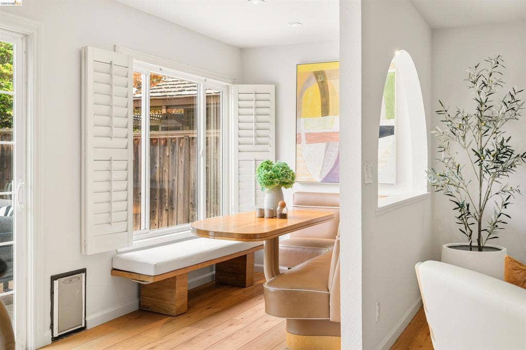 Wood-finish flooring with a built-in bench, window with plantation shutters, sliding glass door, and an arched wall opening