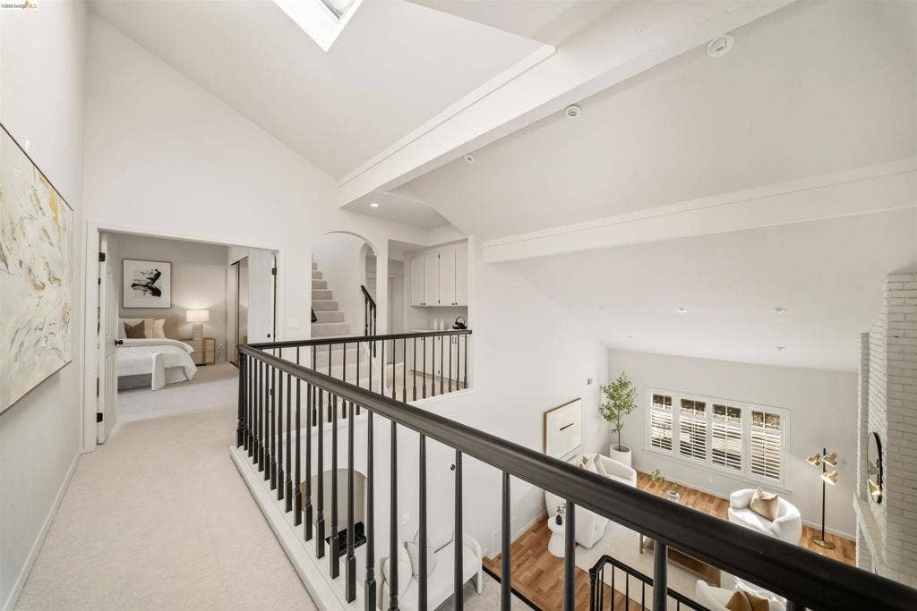 Vaulted ceiling with skylight, white painted brick fireplace, plantation shutters, wood-finish flooring, and white cabinetry
