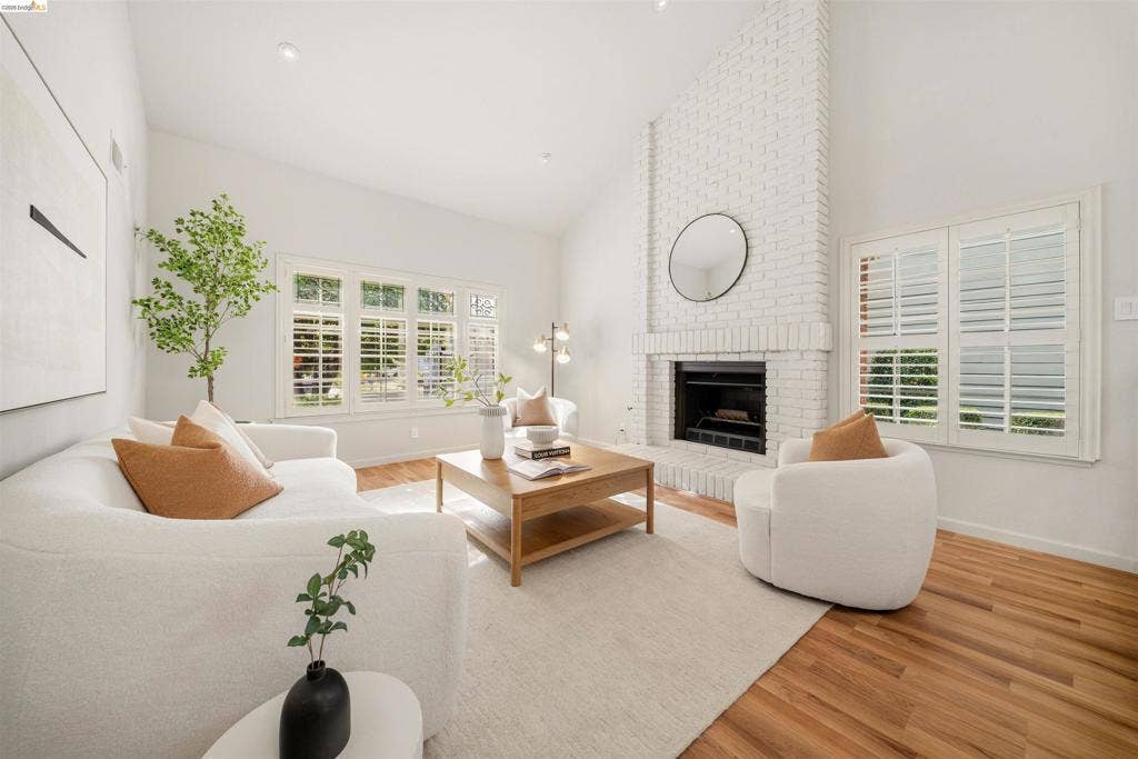 Vaulted ceiling, wood-finish flooring, white brick fireplace, multiple windows with plantation shutters, recessed lighting