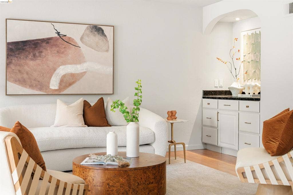 White painted cabinetry with dark stone countertop, wood-finish flooring, and arched entryway