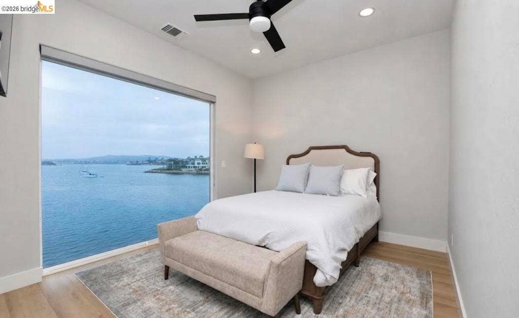 3944 Lighthouse Pl, Discovery Bay, CA 94505 Primary Bedroom with Floor-to-Ceiling Window Overlooking Waterfront Serene waterfront primary bedroom featuring a large picture window framing expansive water views, wood-finish flooring, neutral wall finishes, and a ceiling fan
