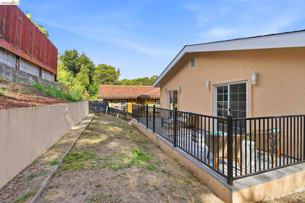 Outdoor patio with black metal railing, two sliding glass doors, stucco exterior, and wall-mounted exterior lighting
