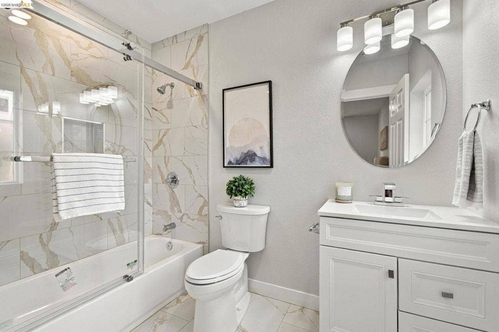 White vanity with integrated sink, circular mirror, and multi-bulb light fixture