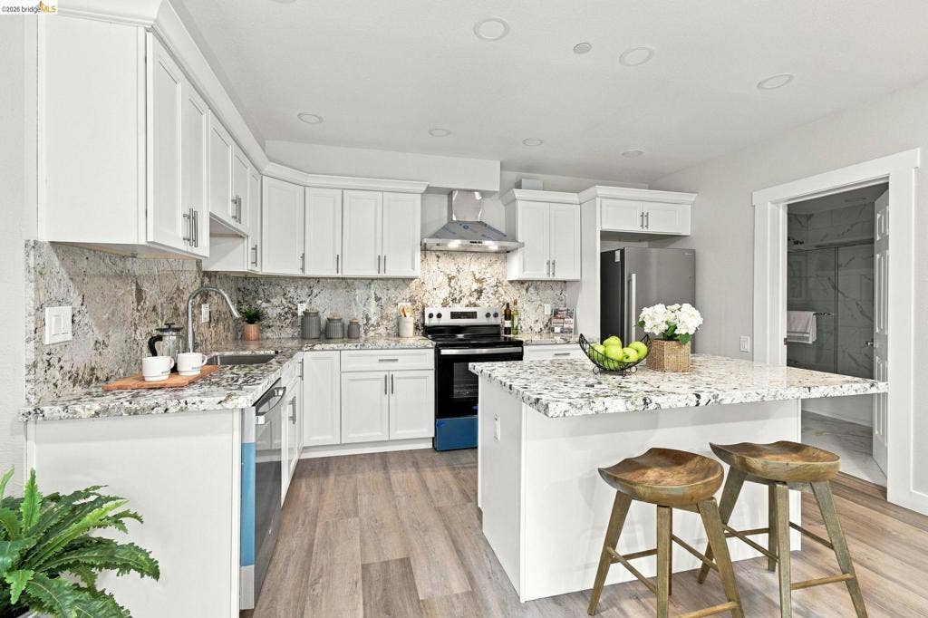 Kitchen featuring white cabinetry, stone countertops, stainless steel appliances, a center island with seating, and wood-finish flooring