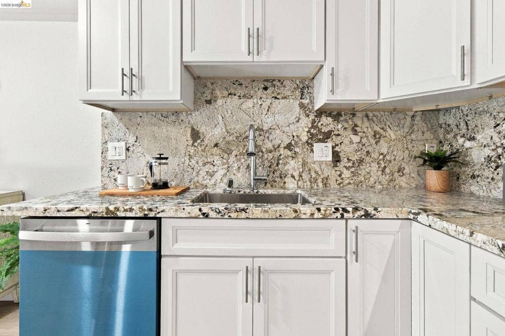 White shaker-style cabinetry, stainless steel sink with a gooseneck faucet, integrated dishwasher, and granite countertops with matching full-height backsplash