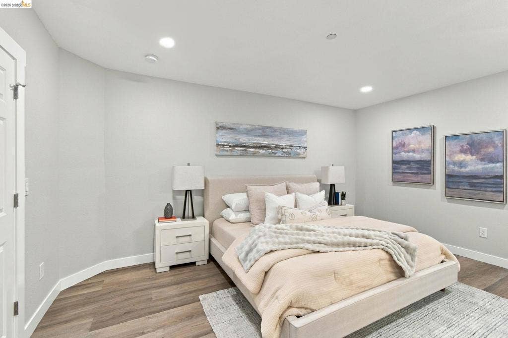 Recessed lighting, wood-finish flooring, white trim, and a white interior door