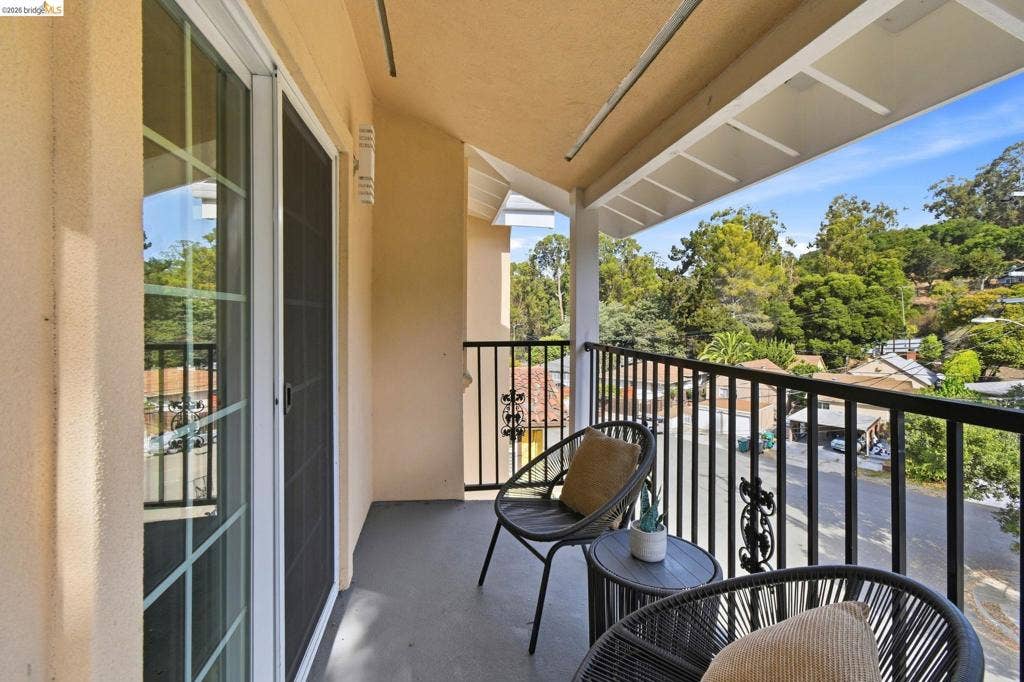Outdoor balcony with painted concrete flooring, white overhead beam structure, and black metal railing