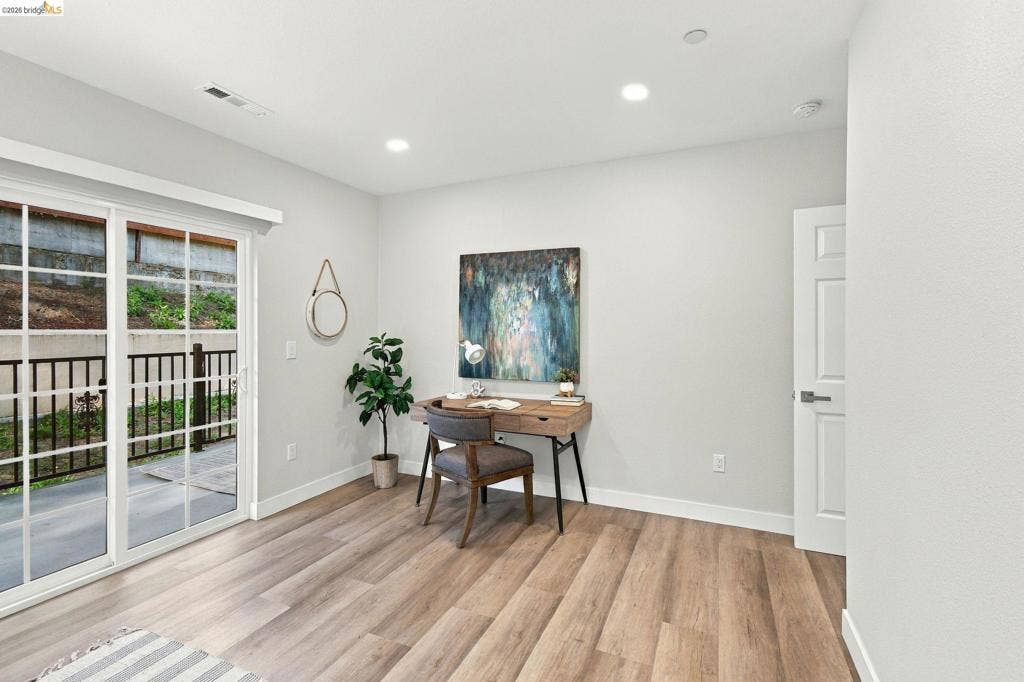 Recessed lighting, wood-finish flooring, white trim, sliding glass door with grid pattern, and white interior door with contemporary hardware