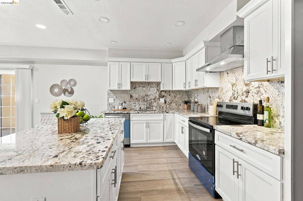 Kitchen featuring white cabinetry, granite countertops, stainless steel appliances, wood-finish flooring, and recessed lighting
