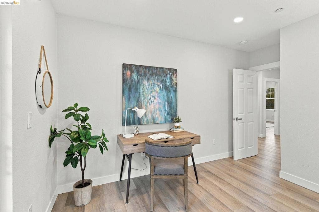 Wood-finish flooring, recessed ceiling lighting, light gray wall paint, white trim, and a paneled interior door