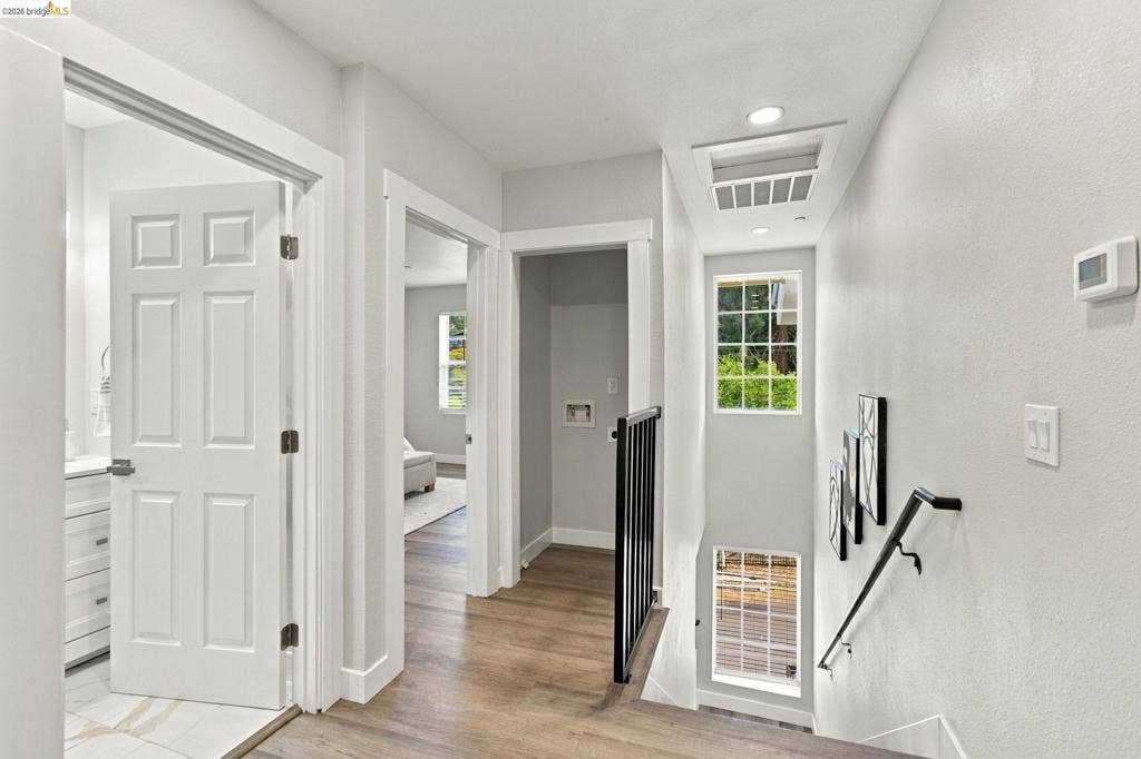 Wood-finish flooring, white paneled doors, black metal handrails, and recessed lighting