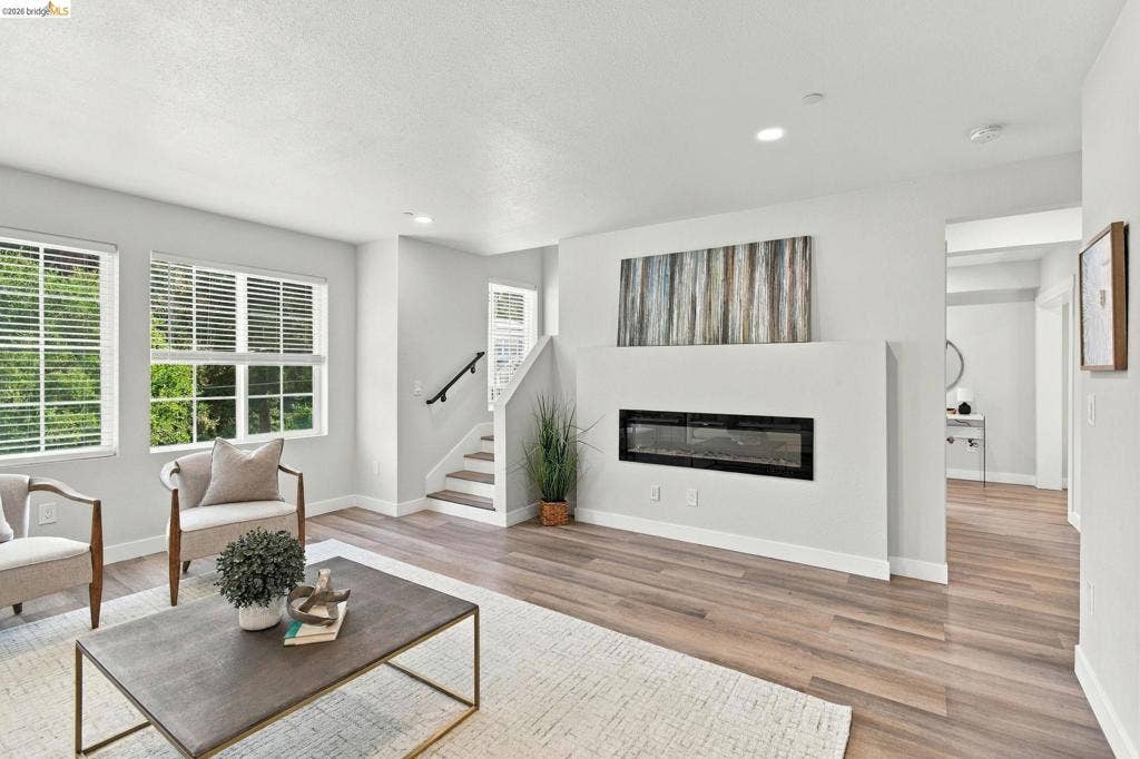 Spacious living area featuring wood-finish flooring, multiple windows with blinds, a built-in fireplace, and recessed lighting