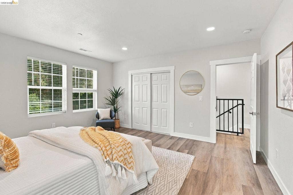Dual windows with blinds, wood-finish flooring, recessed lighting, double-door closet, and black metal stair railing