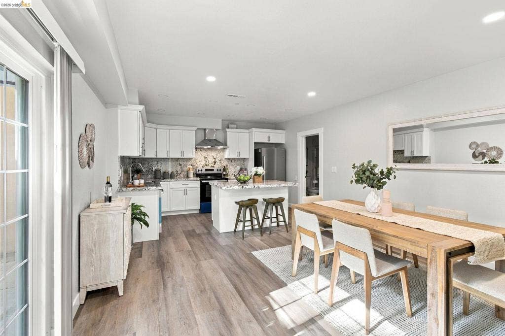 Open-concept living space featuring wood-finish flooring, recessed lighting, and a white kitchen with an island