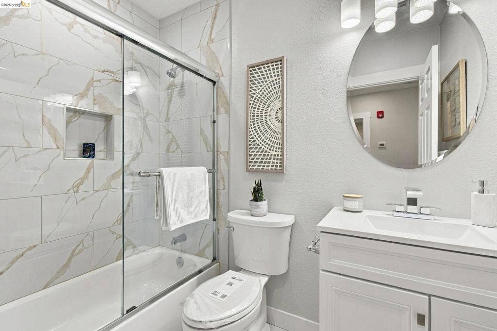 Bathtub with sliding glass enclosure, integrated shower niche, and large format wall tile