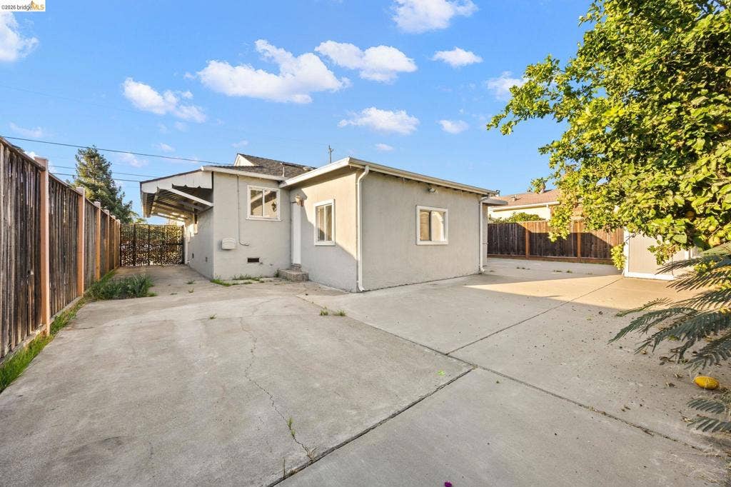 2240 Lessley Ave, Castro Valley, CA 94546 Expansive concrete paving, stucco exterior, multiple windows, and a wood privacy fence