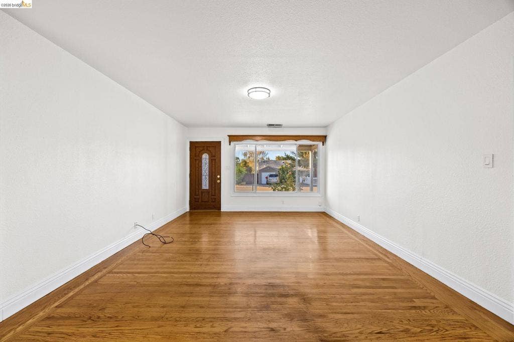 2240 Lessley Ave, Castro Valley, CA 94546 Wood-finish flooring, white walls, decorative front door with clear glass panels, bay window with wood trim, and a flush-mount ceiling light fixture