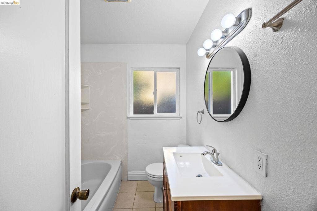2240 Lessley Ave, Castro Valley, CA 94546 White vanity with an integrated sink, a large round mirror, and a window for natural light